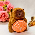 Brown teddy bear with an orange and a gold bottle on a white surface with pink flowers in the background