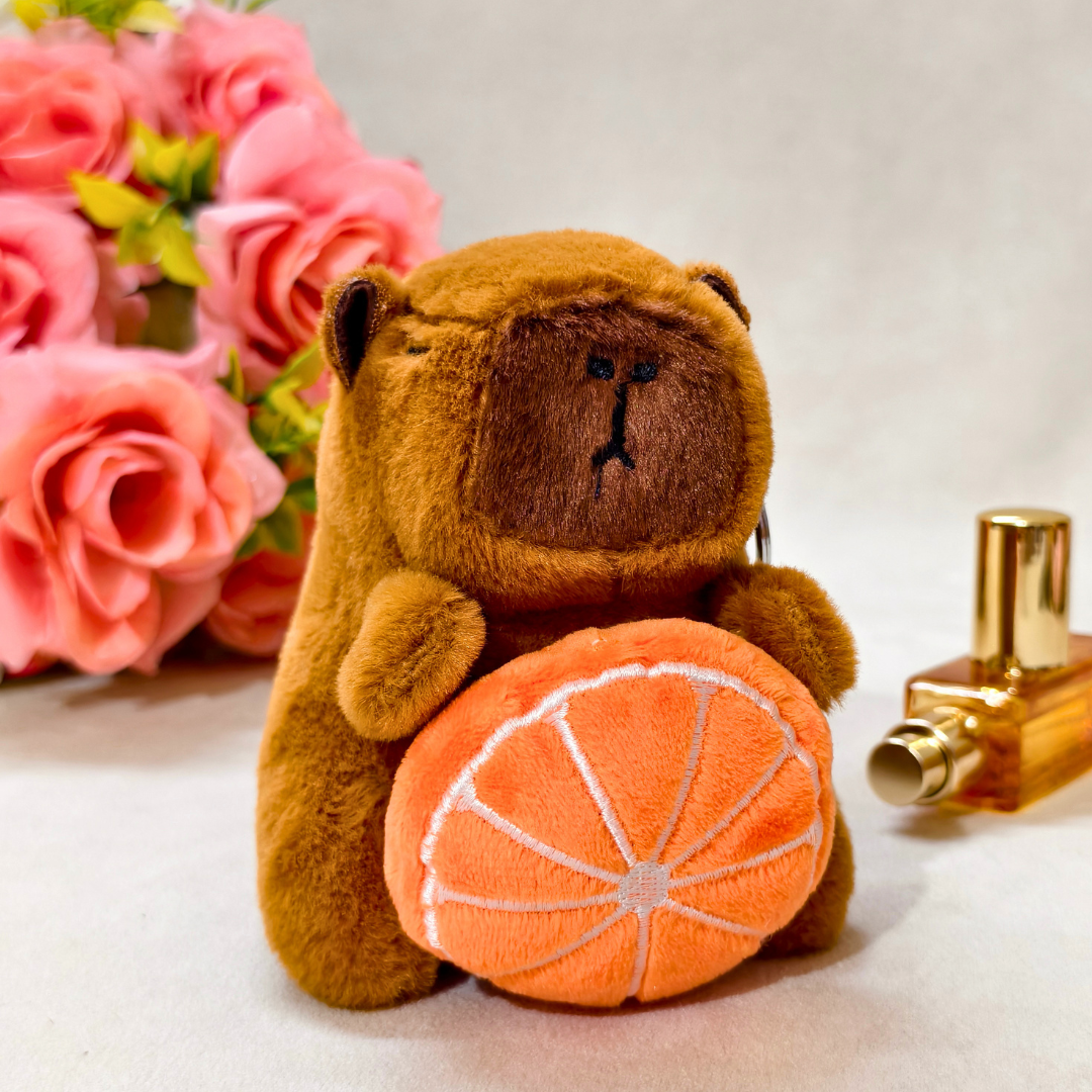 Brown teddy bear with an orange and a gold bottle on a white surface with pink flowers in the background