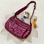 Maroon handbag with a strap, small figurine, and bottle on a decorative doily.