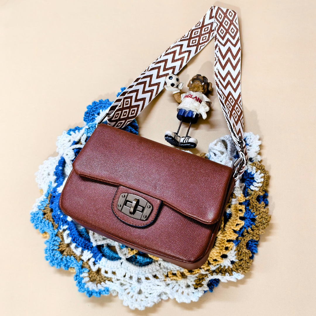 Brown handbag with a patterned strap on a textured surface
