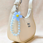 Blue flower keychain with beads attached to a beige handbag.