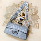 Blue textured handbag with a patterned strap on a decorative leaf background
