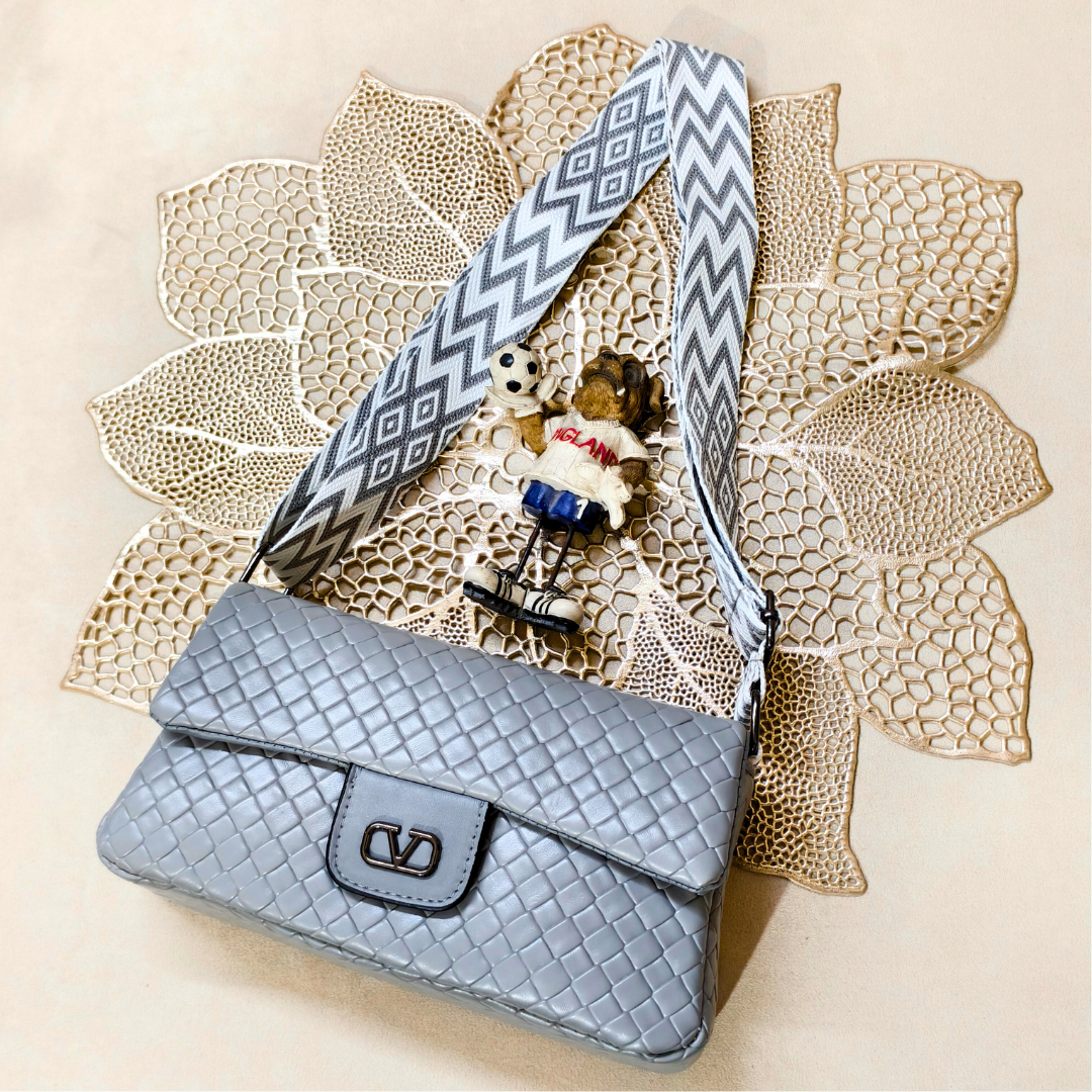 Blue textured handbag with a patterned strap on a decorative leaf background
