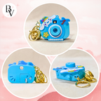 Blue camera-shaped keychain with a gold chain on a pink background