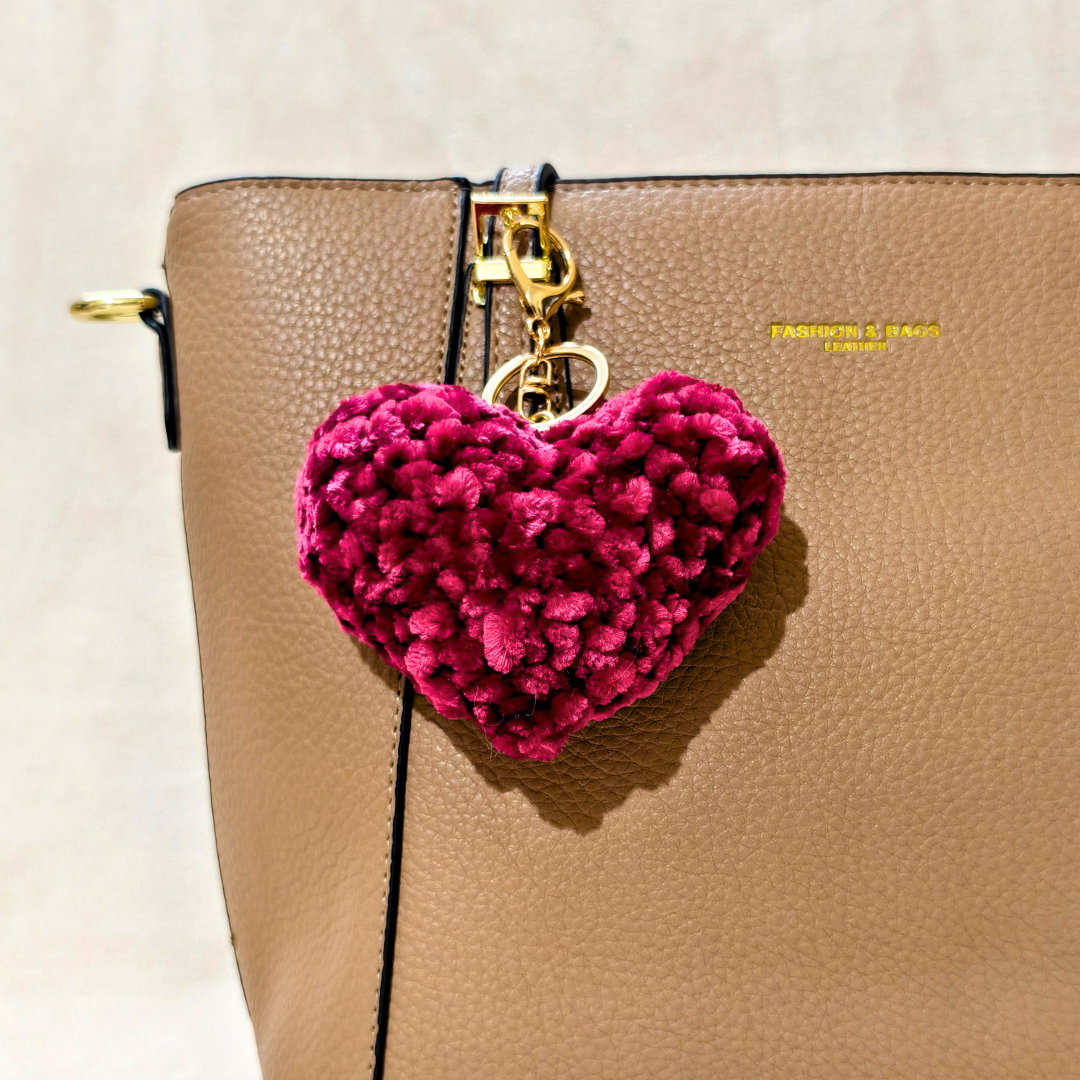 Pink heart-shaped keychain attached to a beige handbag.