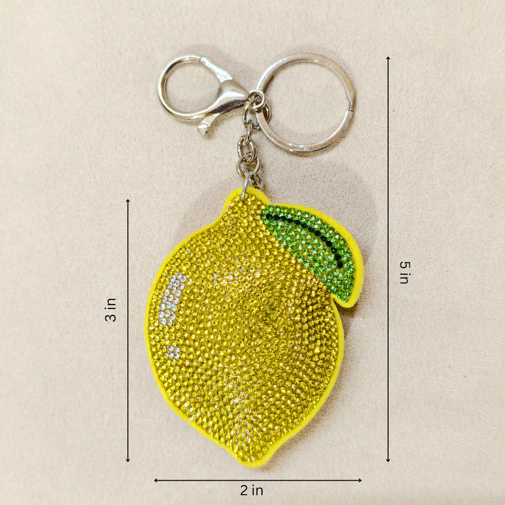 Yellow lemon-shaped keychain with rhinestone details on a beige background