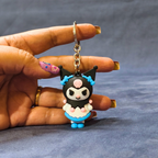 Hand holding a small black and blue character keychain against a gray background