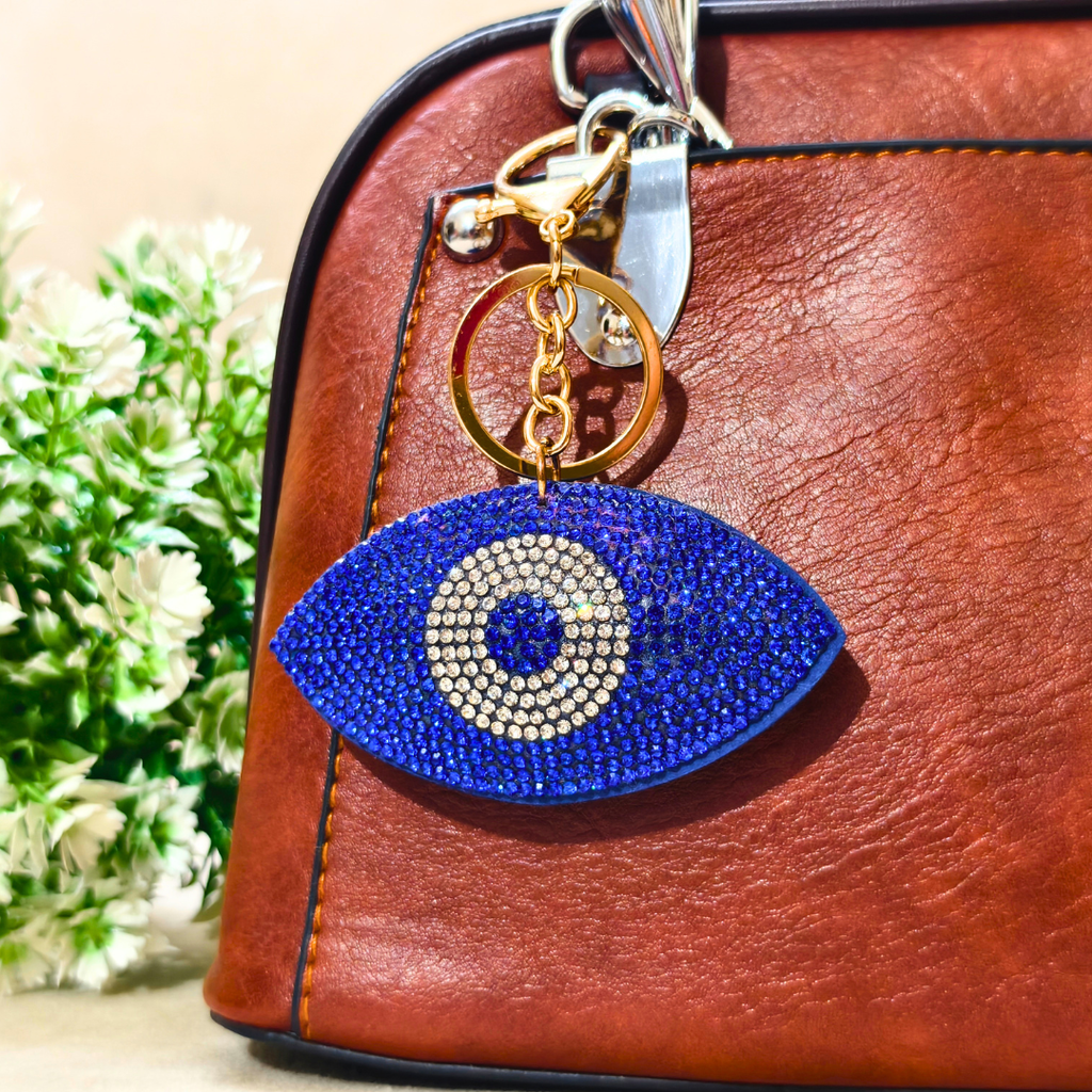 Blue evil eye keychain with gold accents on a brown leather bag