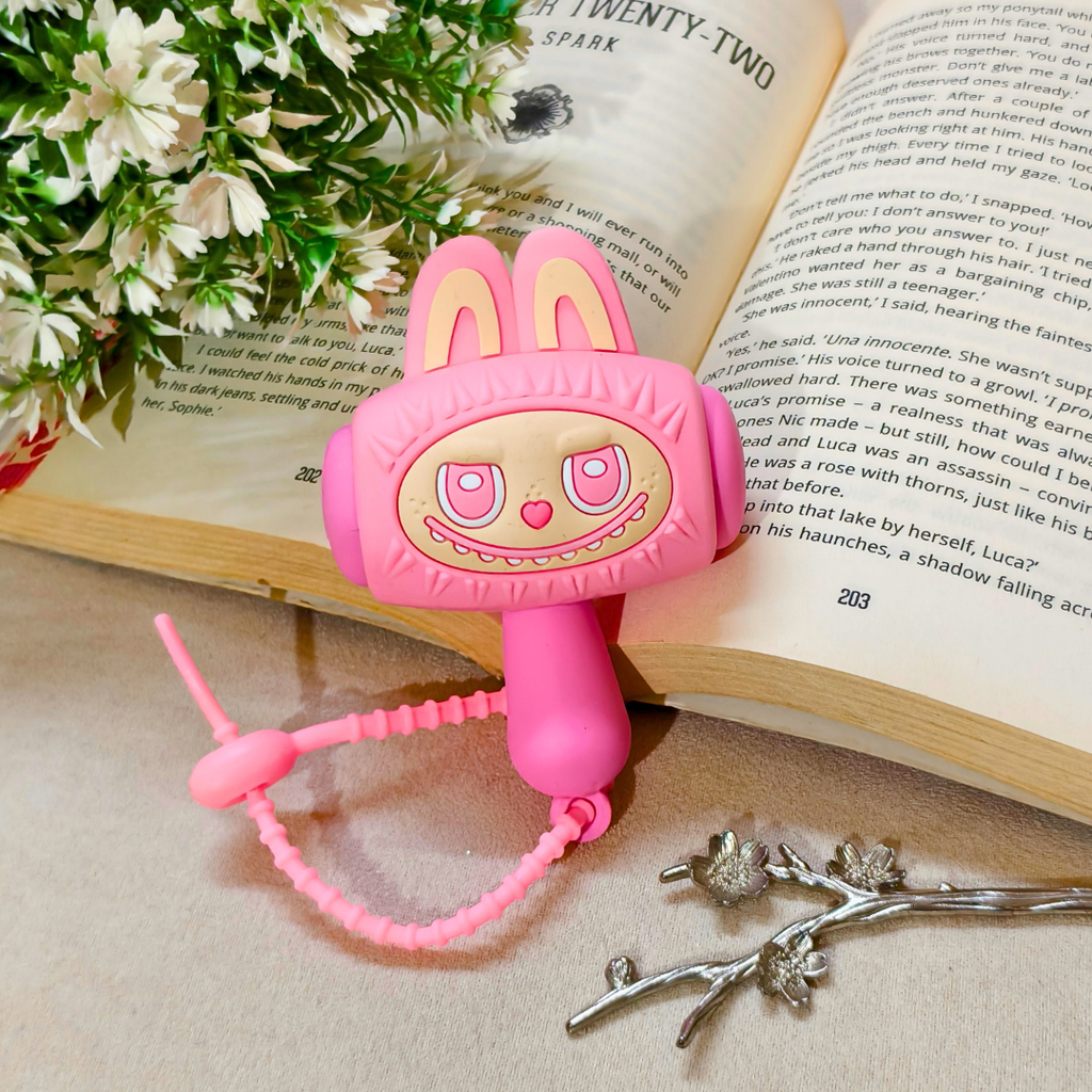 A pink bunny-shaped hair clip with a cute face and a matching pink beaded wrist chain, styled on an open book with white flowers in the corner.
