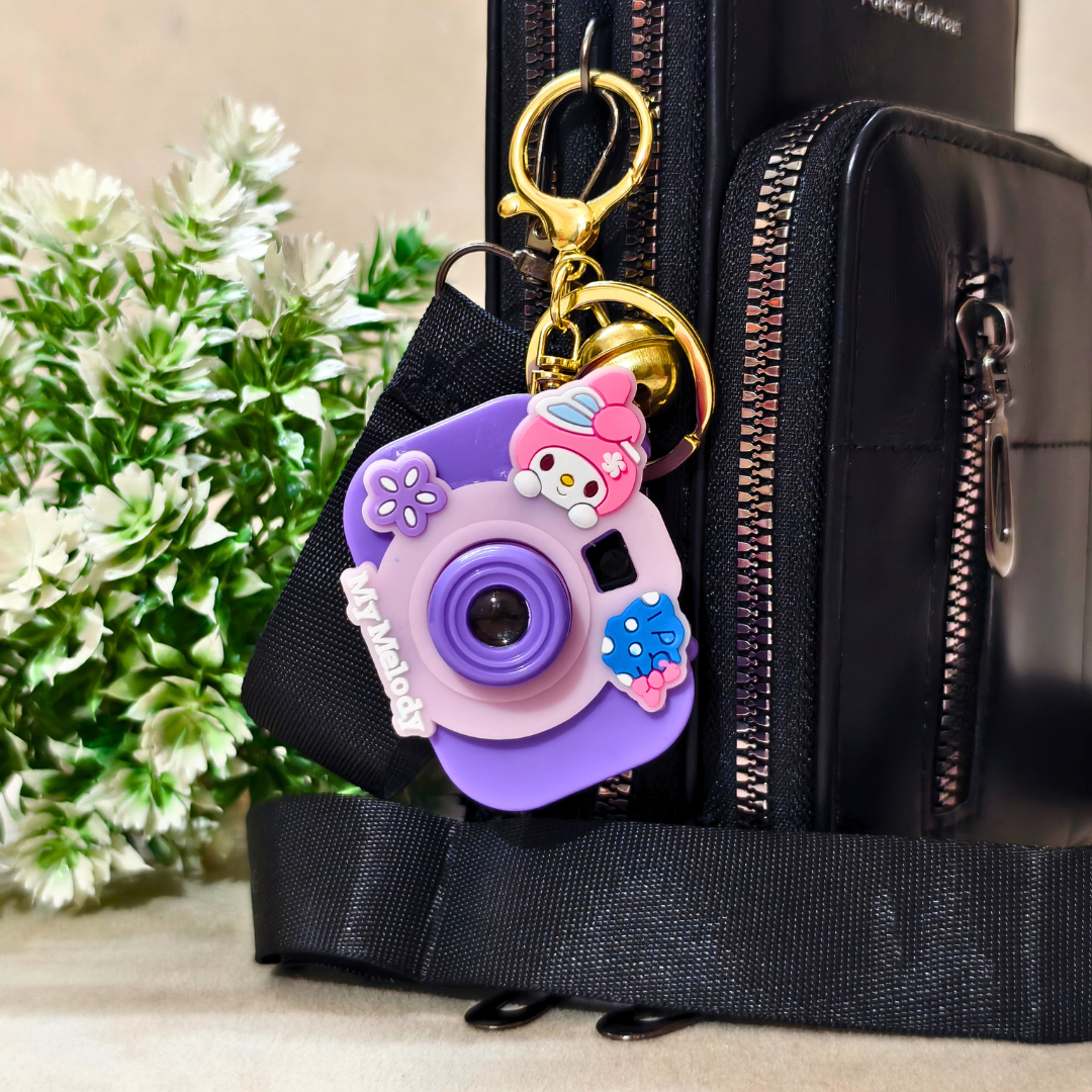 Black bag with a purple camera-shaped keychain featuring a cartoon character, against a neutral background.