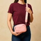 A woman wearing a maroon t-shirt and blue jeans models a small pink crossbody bag with a patterned pink and white strap. The bag has a silver zipper and a small 'Society' brand logo on the front.