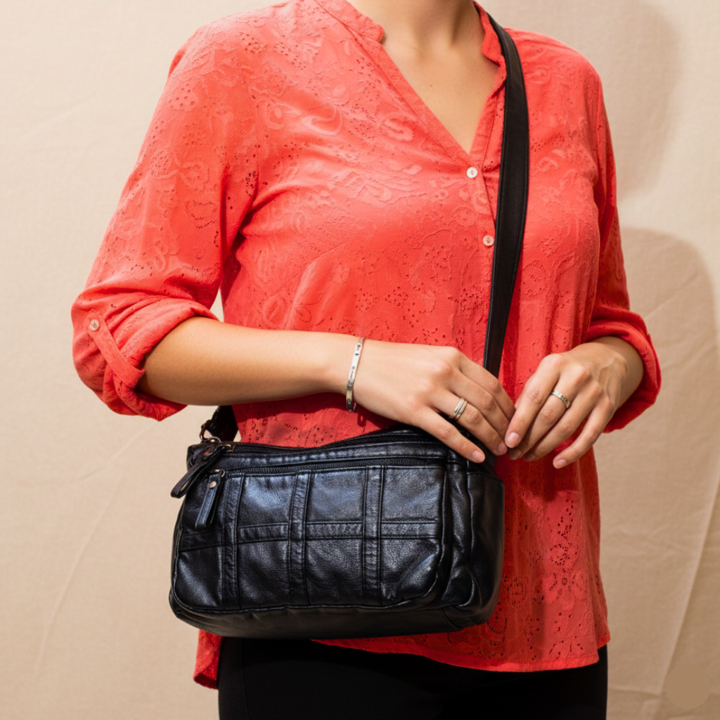 Person wearing a red shirt holding a black leather bag against a beige background