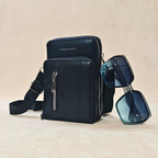 Black leather crossbody bag with sunglasses on a beige background