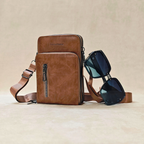 Brown leather crossbody bag with sunglasses on a beige background