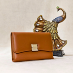 Brown wallet with gold clasp in front of a decorative peacock statue on a beige background