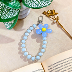 Blue Flower Phone Charm With Props In Front Of Beige Background
