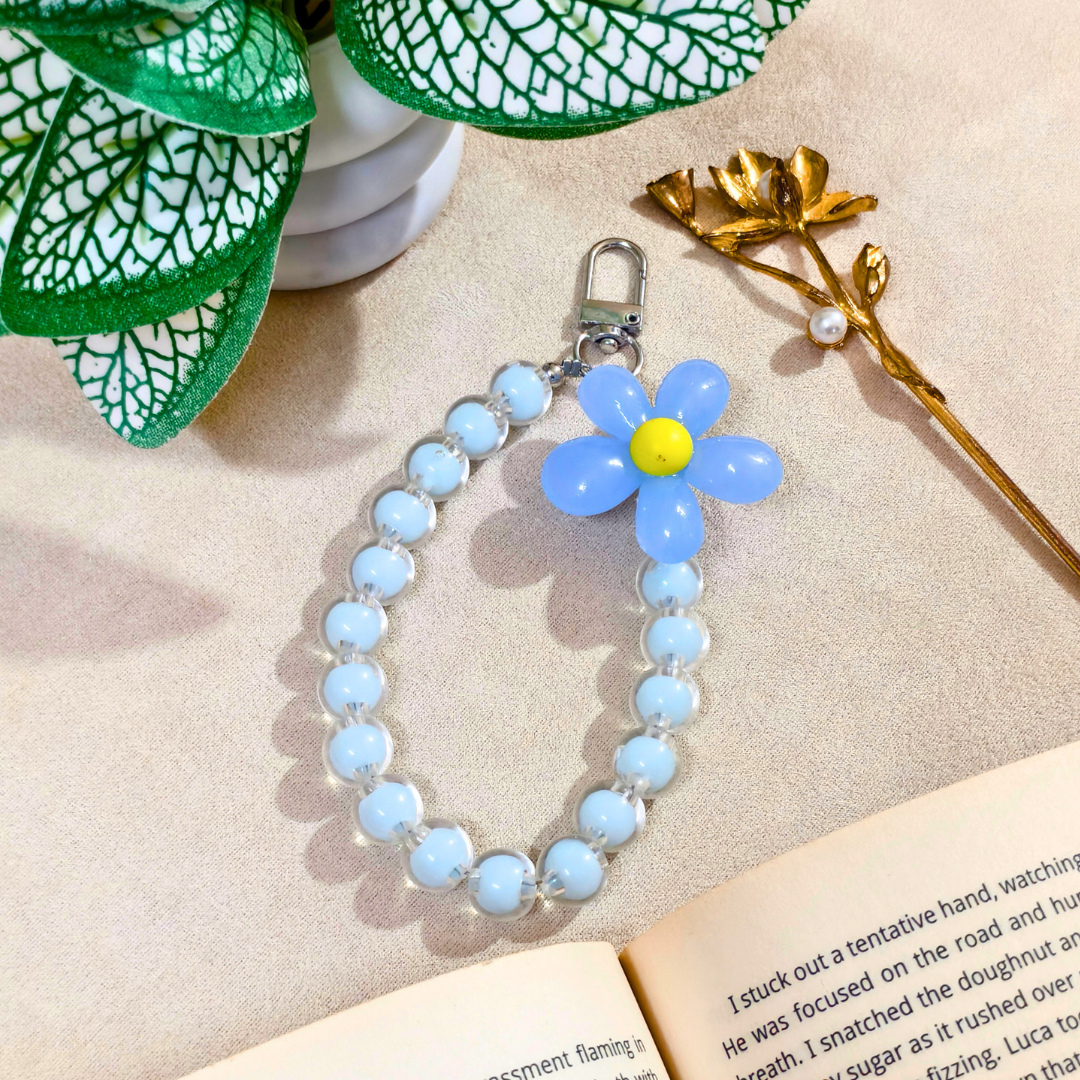 Blue Flower Phone Charm With Props In Front Of Beige Background