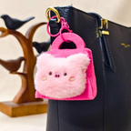 Pink fluffy keychain attached to a black handbag with a blurred background