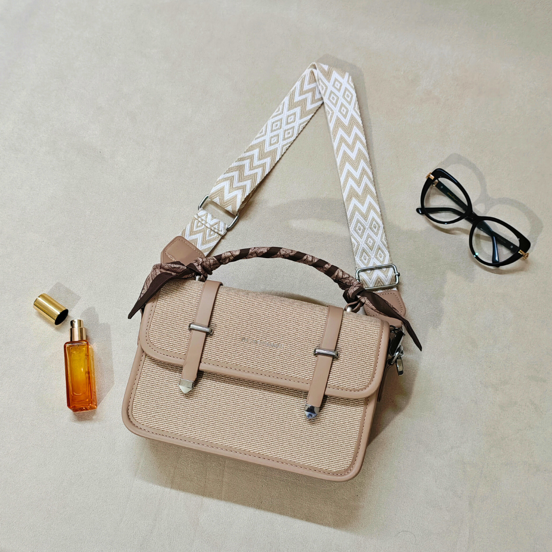 Beige woven handbag with satin wrapped handle and sunglasses on a beige background