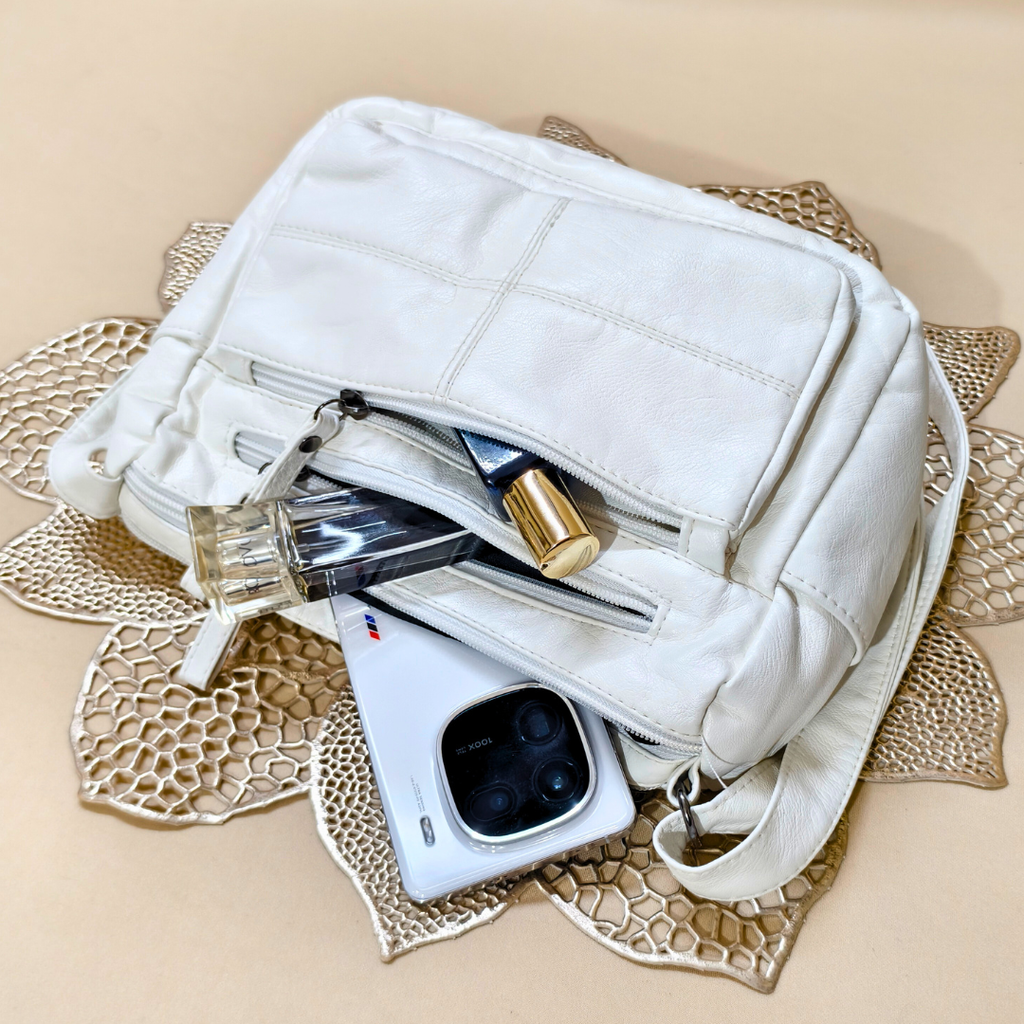 White handbag with a phone, perfume bottle, and other items on a decorative mat.