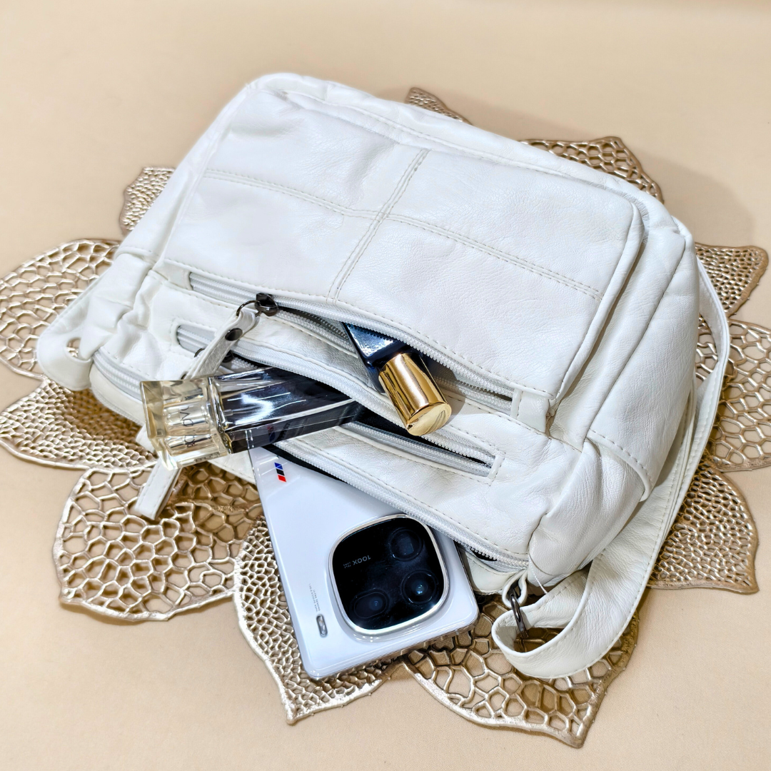 White handbag with a phone, perfume bottle, and other items on a decorative mat.