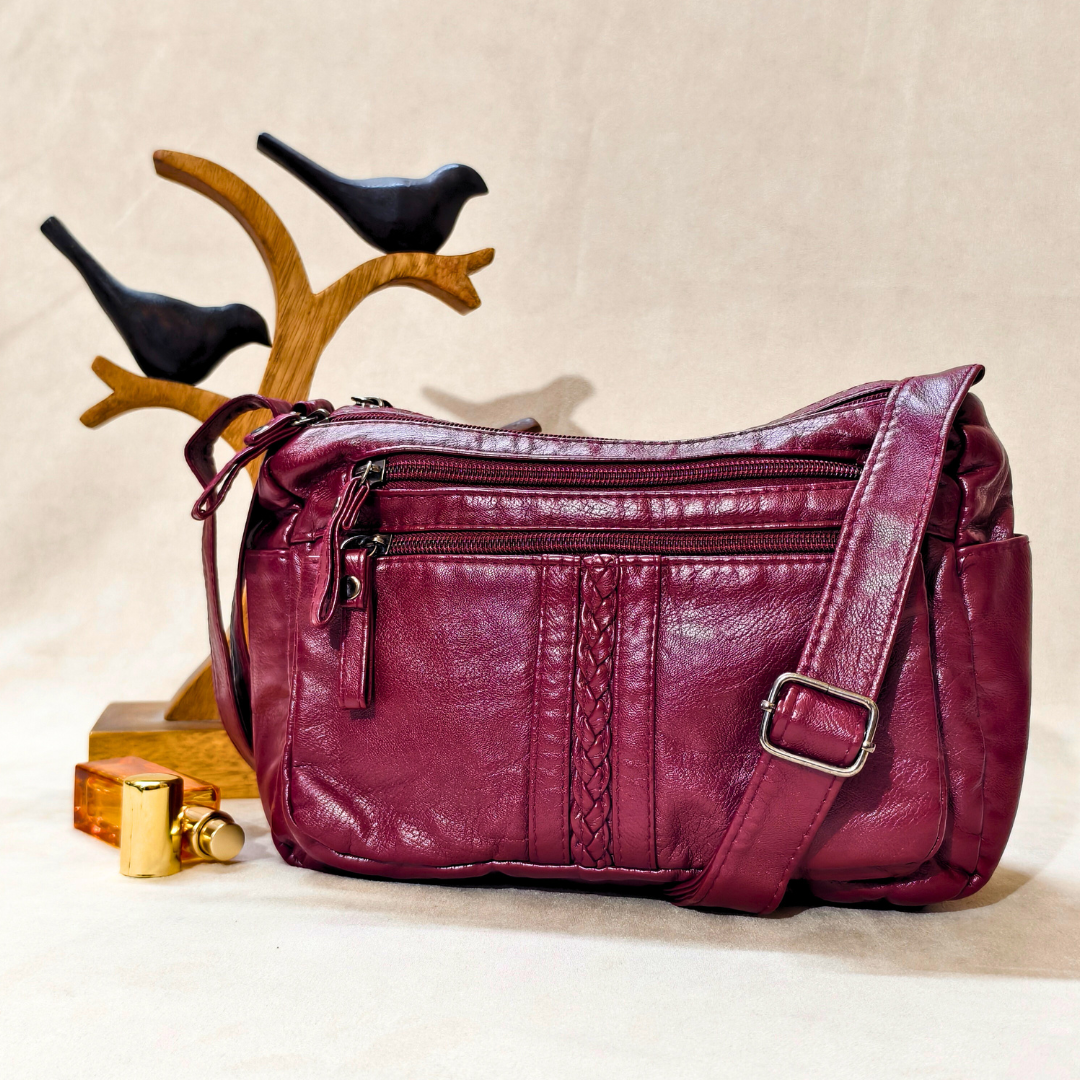 Purple leather handbag on a beige background with decorative birds and a perfume bottle.