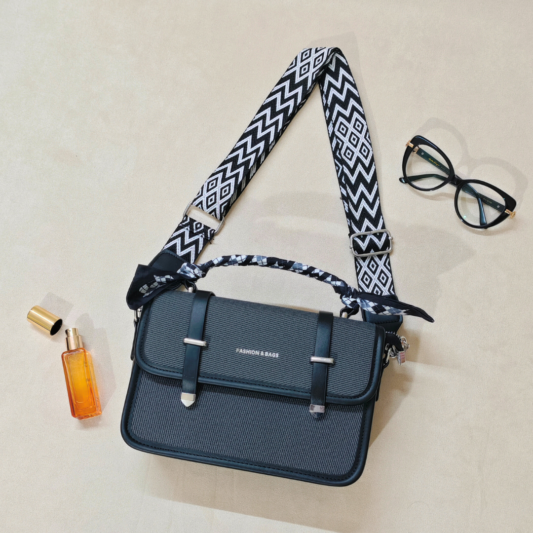 black sling bag on top of a beige background alongside a bottle of perfume and a pair of glasses.