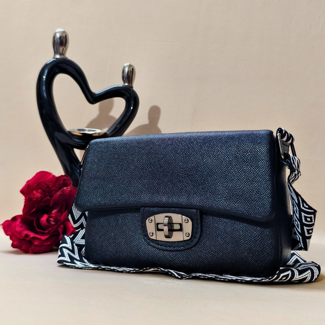 Blue handbag with a decorative strap next to a red rose on a beige background