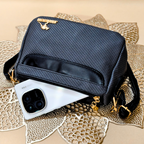 Black textured handbag with gold accents on a textured beige surface