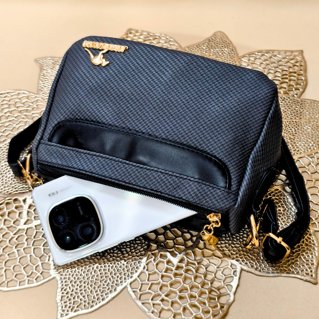Black textured handbag with gold accents on a textured beige surface