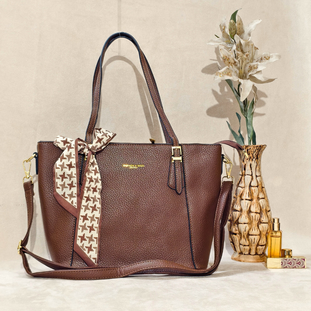 Brown handbag with a decorative ribbon on a beige surface with a vase and flowers in the background.