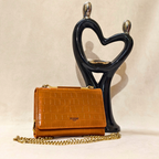 Brown handbag with gold chain and 'Pierre' brand name on a beige background with a black heart-shaped sculpture.
