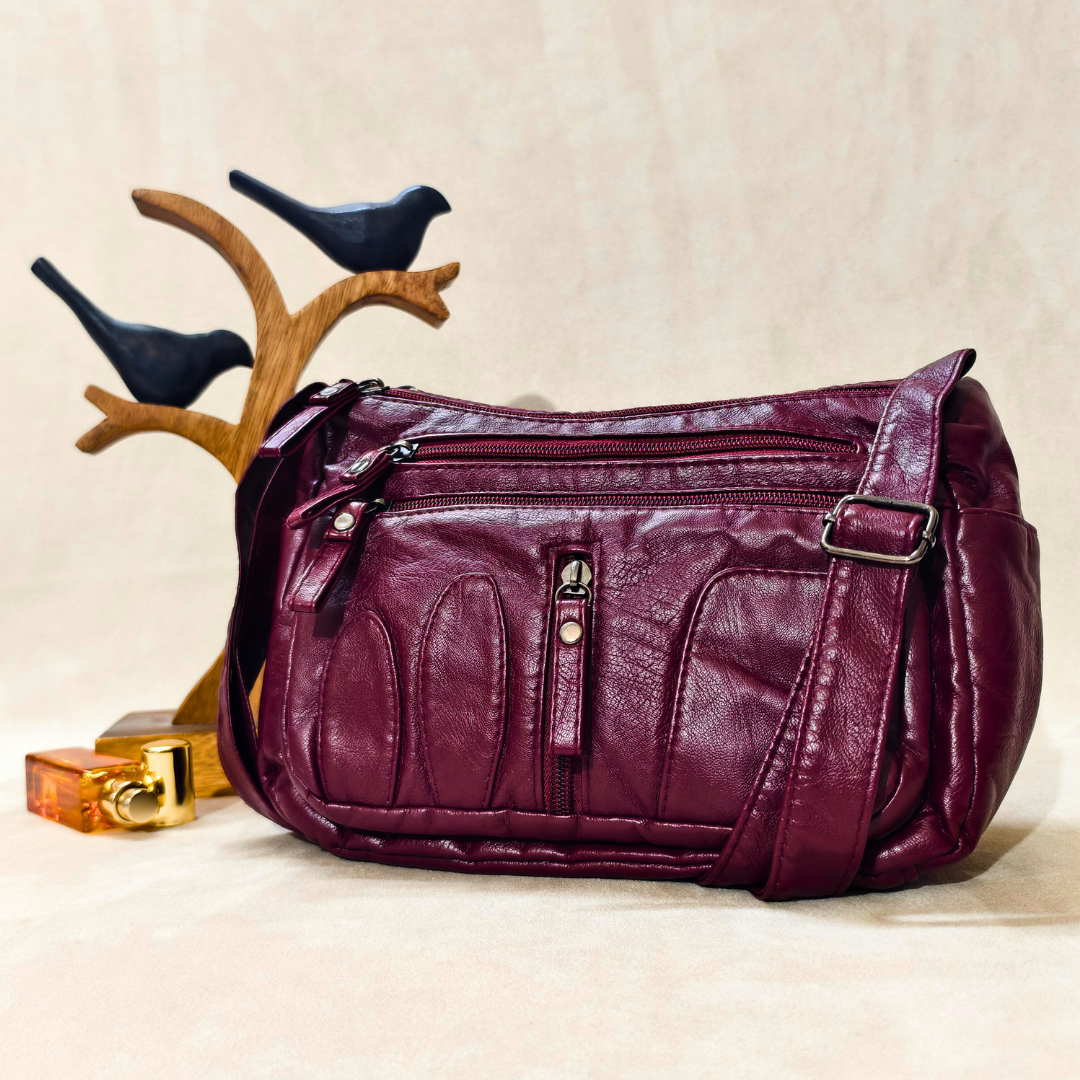 Purple leather handbag on a beige surface with decorative birds and a perfume bottle.