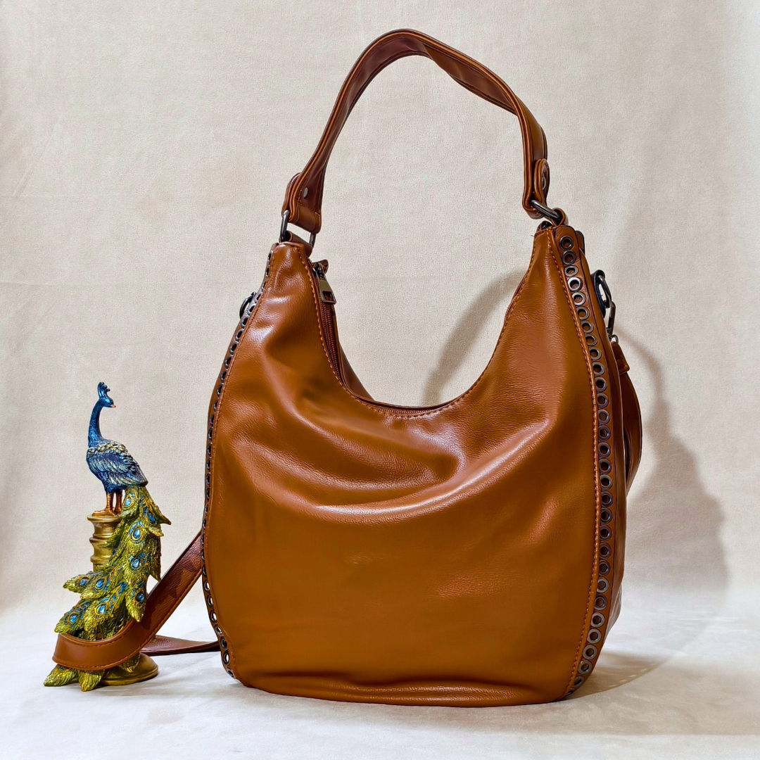 Brown leather handbag with decorative peacock charm on a beige background