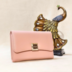 Pink wallet with gold clasp next to a decorative peacock figure on a beige background