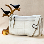 White quilted handbag with a strap on a beige surface, with decorative birds in the background.