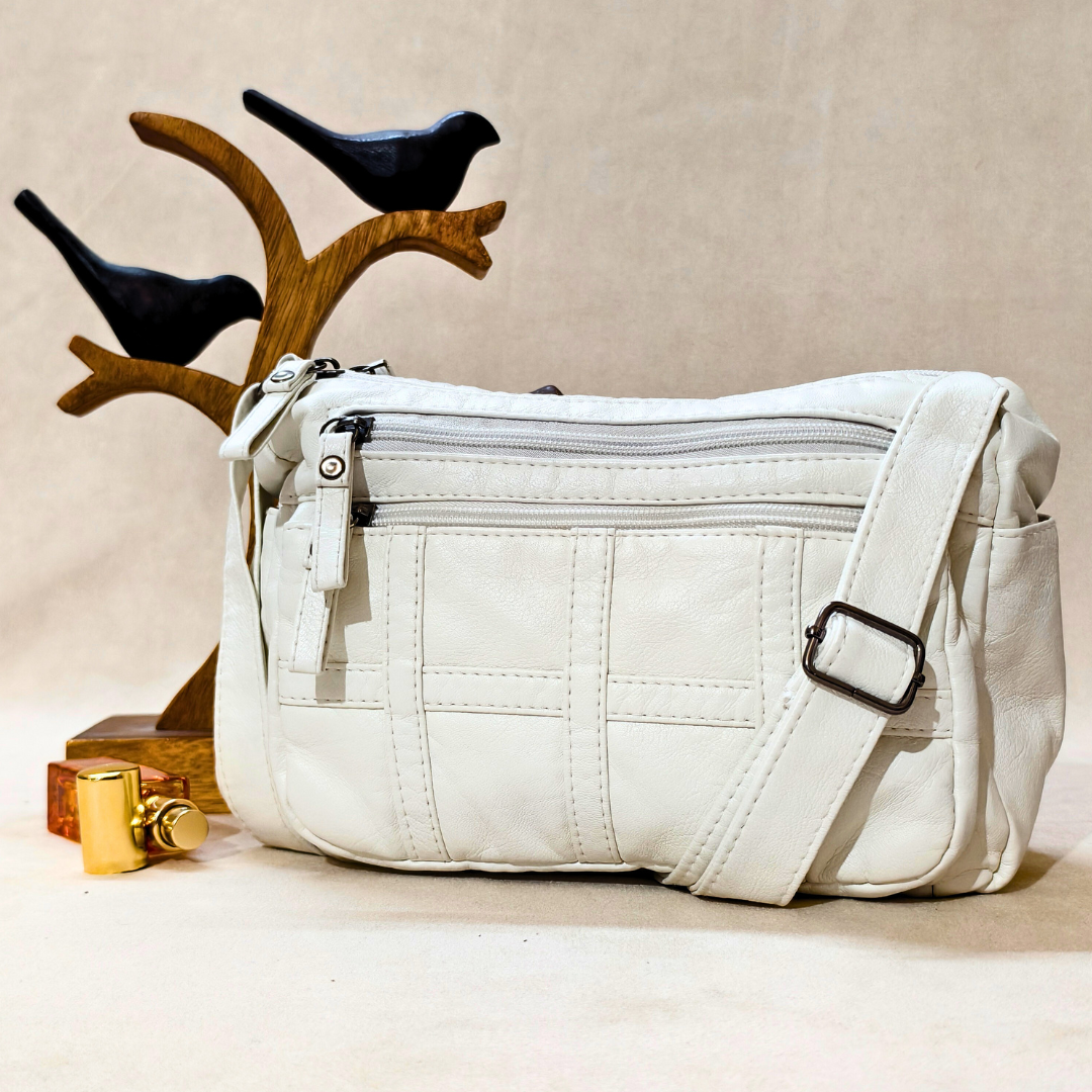White quilted handbag with a strap on a beige surface, with decorative birds in the background.
