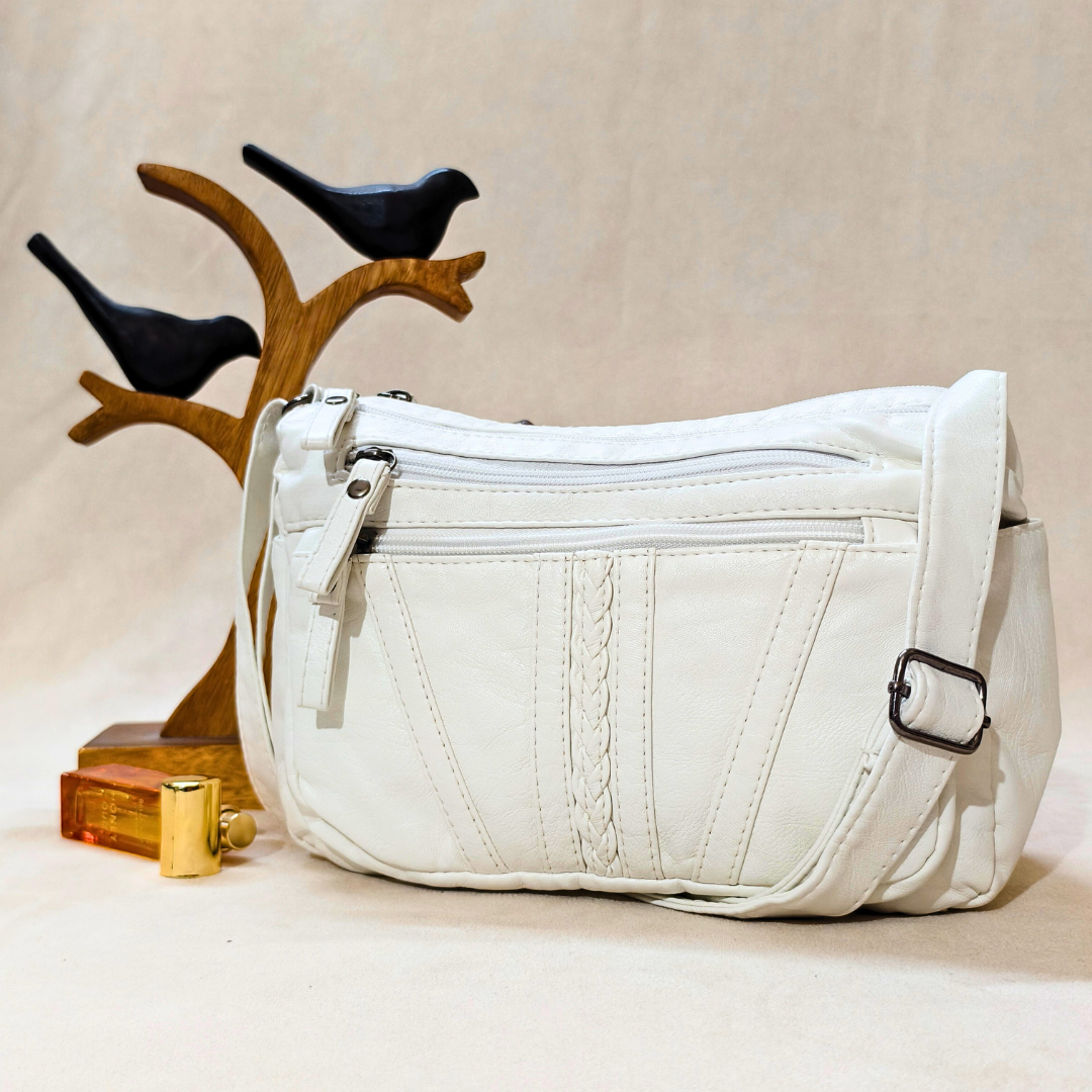White leather crossbody bag on a beige surface with decorative birds in the background