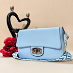 Light blue handbag with a zigzag strap next to a red rose and black heart-shaped object on a beige background