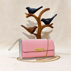 Pink handbag with gold chain and gray base, placed on a wooden bird stand against a beige background.