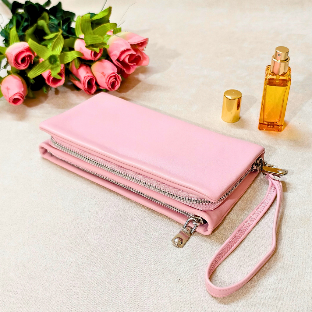 Pink wallet with a chain strap on a light surface with pink roses and a gold bottle.