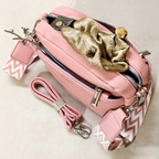 A pink pebbled leather crossbody bag with silver-tone hardware, a matching pink and white chevron-patterned strap, and a gold scrunchie accessory placed on top, shown on a light beige background.