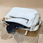 White handbag with sunglasses and a decorative item on a textured beige surface