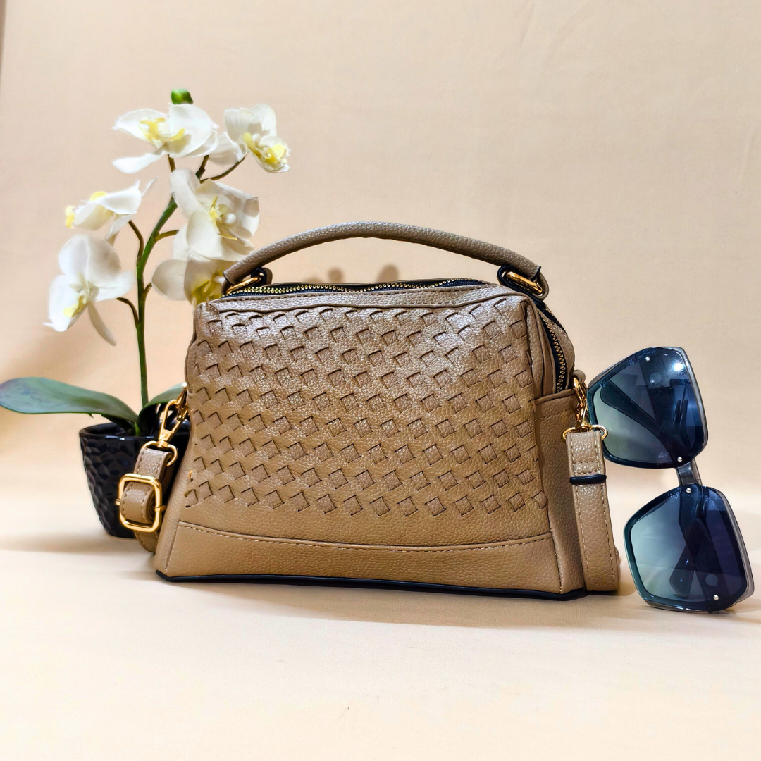 Beige woven handbag with a strap, accompanied by blue sunglasses and a small plant on a beige background