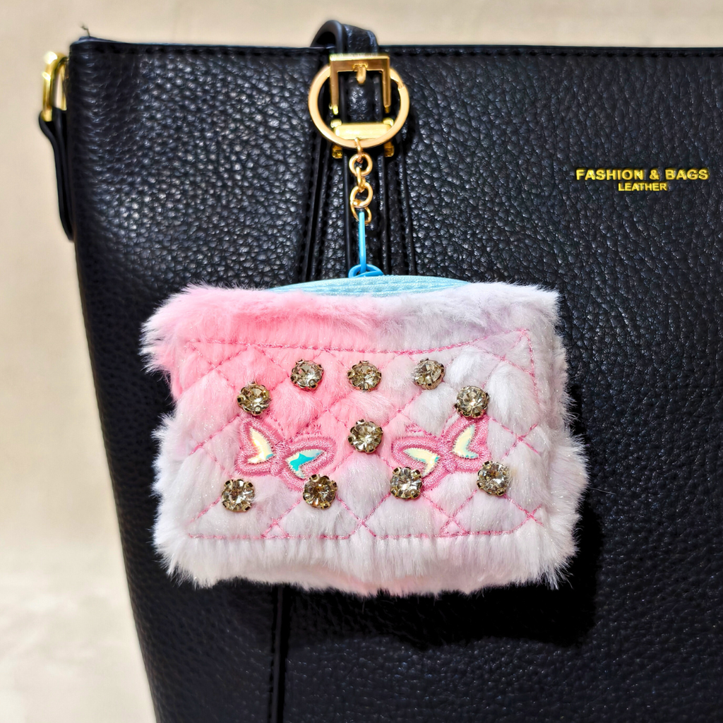 Pink and white quilted pouch with decorative elements attached to a black bag.