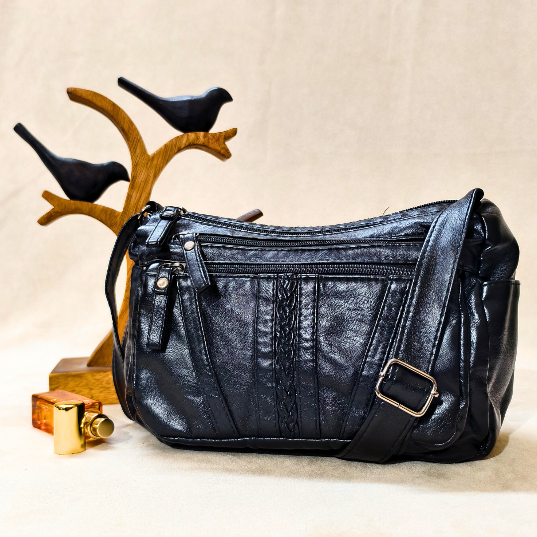 Black leather handbag on a beige surface with decorative birds and a wooden stand in the background.