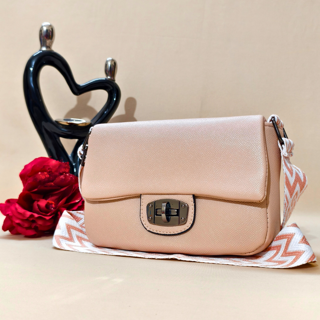 Beige handbag on a beige surface with red flowers and a black heart-shaped object in the background.