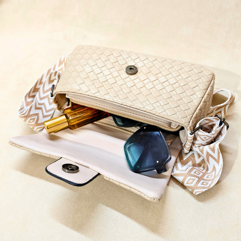 Beige woven handbag with sunglasses and a phone inside on a beige background