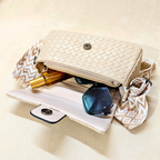 Beige woven handbag with sunglasses and a phone inside on a beige background