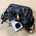 Black leather bag with a phone and lipstick on a textured surface